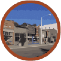 Central Region of Morgan Valley. A circular traffic mirror reflecting a quiet urban street scene with buildings, a clear sky, and an intersection, bordered by a contrasting orange frame, highlighting the importance of traffic safety and urban design.