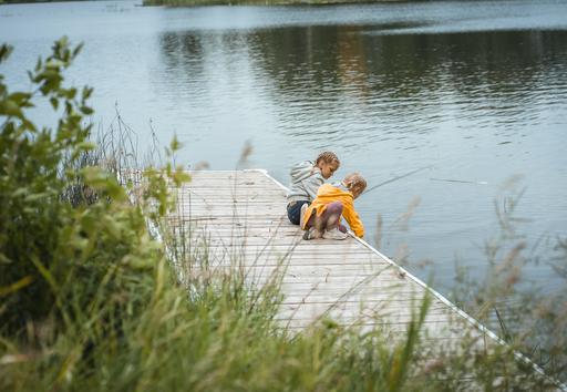 Two children fishing from a dock at a lake.